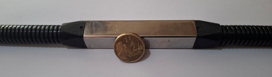 A single sensor node: a short square stainless tube between two conduit ends, beside a two-dollar coin for scale